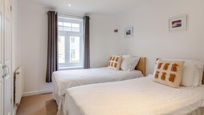 Et hotelværelse med to senge, et vindue med gardiner, en radiator og et lille billede på væggen.