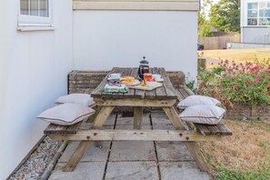 A wooden picnic table with cushions, a book, a cup, and a teapot. - 4 Bed in Newquay (oc-a45833) (Black Cross)