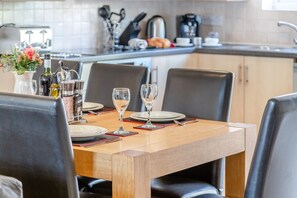 A dining table set with plates, wine glasses, and cutlery, surrounded by chairs. - 4 Bed in Newquay (oc-a45833) (Black Cross)