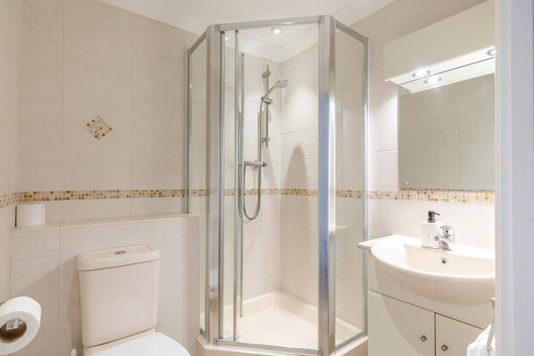 Een moderne badkamer met een douche in een glazen cabine, een toilet en een wastafel met spiegel.