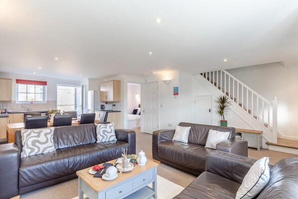 A modern living room with two leather sofas, a coffee table, and a staircase leading to an upper floor. - 4 Bed in Newquay (oc-a45833) (Black Cross)