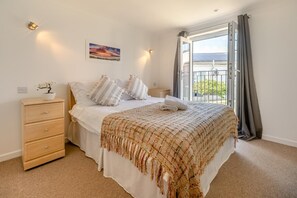 A bedroom with a bed, a nightstand, a dresser, a window with curtains, and a painting on the wall.