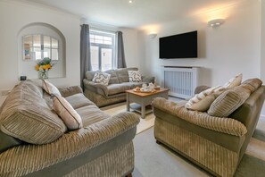 A living room with a sofa set, a coffee table, and a flat-screen TV mounted on the wall. - 4 Bed in Newquay (oc-a45834) (Black Cross)