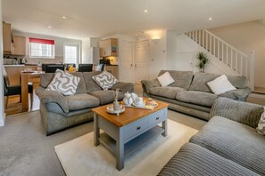 A modern living room with two sofas, a coffee table, and a dining area with a table and chairs. - 4 Bed in Newquay (oc-a45834) (Black Cross)
