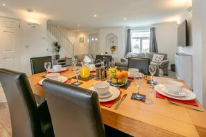 A dining area with a wooden table set for breakfast, including plates, glasses, and a fruit bowl. - 4 Bed in Newquay (oc-a45834) (Black Cross)