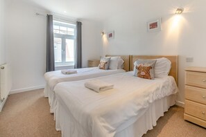 Ein Hotelzimmer mit zwei Betten, einem Heizkörper, einem Fenster mit Vorhängen und einer Wandleuchte.