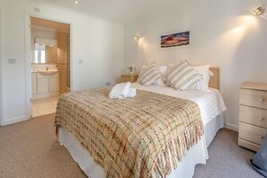A bedroom with a bed, a nightstand, a dresser, and a bathroom visible through an open door.