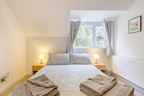 A bedroom with a bed, two bedside tables with lamps, a window with curtains, and a radiator. - 3 Bed in Brancaster (oc-m45869) (Brancaster)