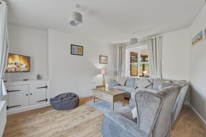 A modern living room with a sofa, a coffee table, a bean bag, and a TV mounted on the wall. - 3 Bed in Brancaster (oc-m45869) (Brancaster)