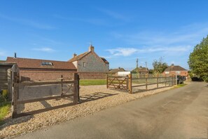 A rural property with a gravel driveway, a stone building, and a metal gate. - 3 Bed in Brancaster (oc-m45869) (Brancaster)