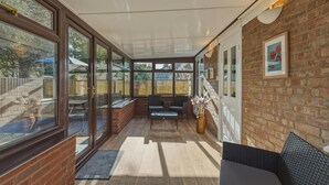 Un patio cubierto con un muro de ladrillo, ventanas grandes y una zona de estar con sillas y una mesa.