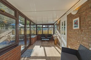 A covered patio with a brick wall, large windows, and a seating area with chairs and a table. - 3 Bed in Brancaster (oc-m45869) (Brancaster)