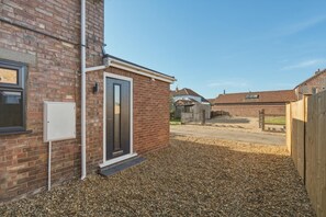 A residential property with a brick exterior, a door, a small window, and a gravel driveway. - 3 Bed in Brancaster (oc-m45869) (Brancaster)