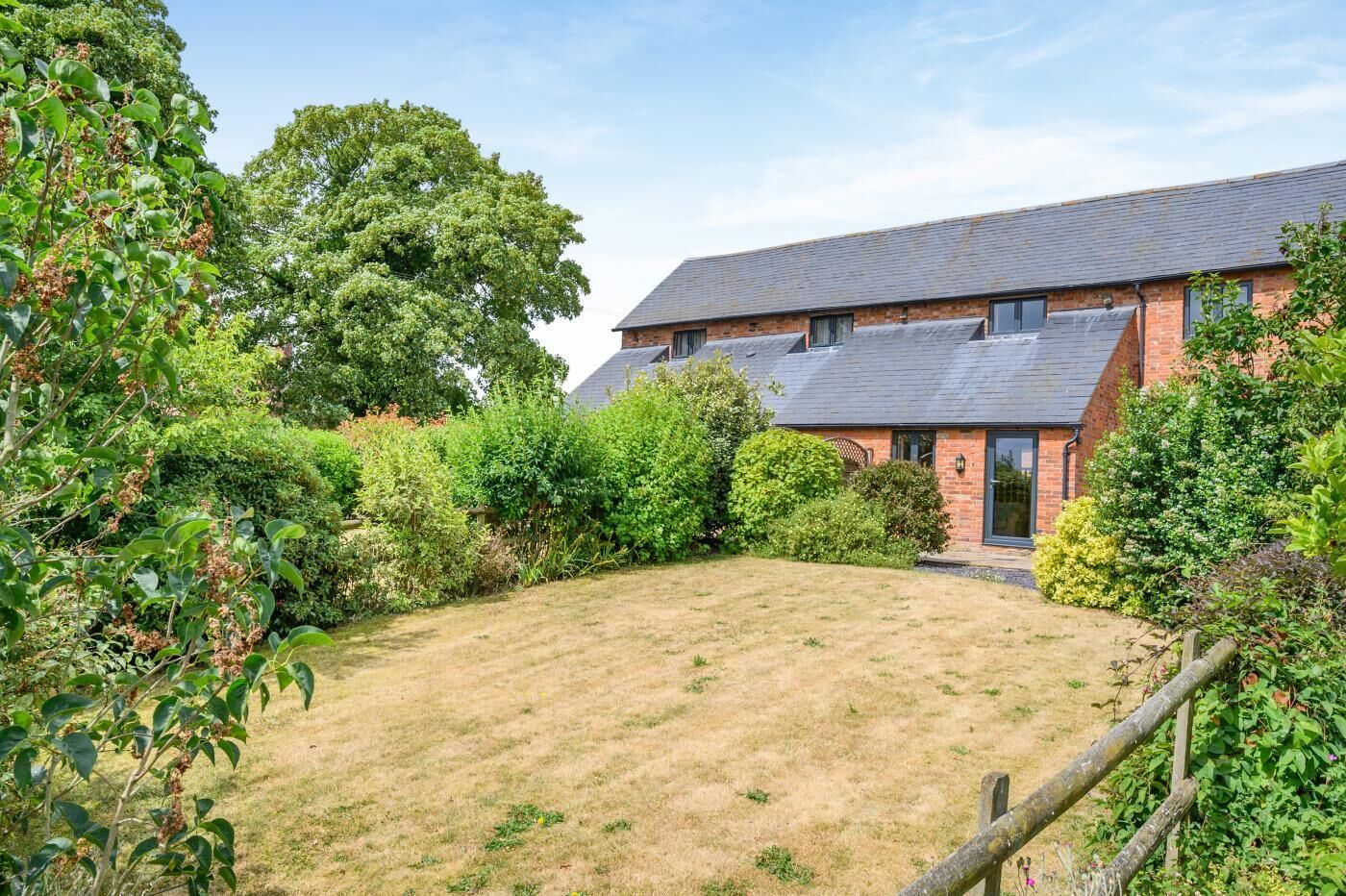 A brick house with a sloped roof, surrounded by a well-maintained lawn and dense shrubbery.