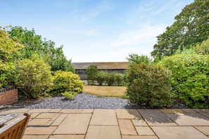 A patio area with stone flooring, a wooden bench, and various shrubs. - 4 Bed in Kenilworth (oc-p45549) (Kenilworth)