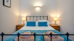 Una cama bien hecha con cabecera, dos lámparas de noche y un cuadro en la pared.