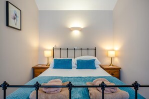 Ein ordentlich bezogenes Bett mit Kopfteil, zwei Nachttischen mit Lampen und einem gerahmten Bild an der Wand.