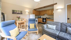 Una sala de estar con un sofá, un sillón y una mesa de comedor con sillas. Se observa una zona de cocina con muebles de madera y electrodomésticos.