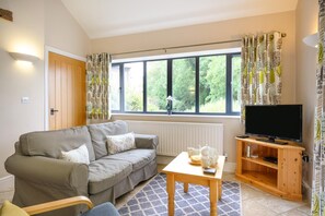 A living room with a sofa, a coffee table, a television on a wooden stand, and a window with curtains. - 2 Bed in Kenilworth (oc-p45550) (Kenilworth)
