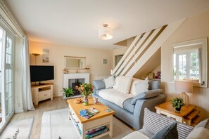 Ein modernes Wohnzimmer mit einer Couch, einem Couchtisch und einem Kamin. Es gibt einen Fernseher, ein Bücherregal und eine Treppe.