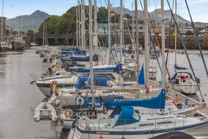 Ein Hafen mit mehreren vertäuten Booten, einige mit Segeln, andere ohne, und einer Berglandschaft im Hintergrund.