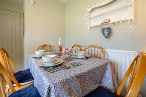 Une table à manger dressée avec de l’assiette, des bols et des couverts blancs, une bouteille de vin rosé et un vase rempli de fleurs.