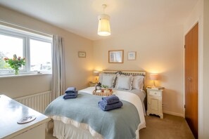 Une chambre à coucher comprenant un lit, des tables de chevet, une fenêtre avec des rideaux, un radiateur et un bureau avec une lampe.