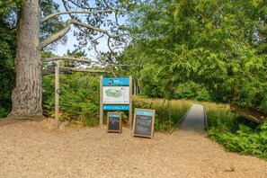 Ein Wegweiser des Wildtierfonds mit Karte und Informationstafel, ein Kiesweg und ein großer Baum.