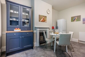 Eine moderne Küche mit einem dunkelblauen Schrank, einem Esstisch mit Stühlen, einer Mikrowelle und einer Uhr an der Wand.