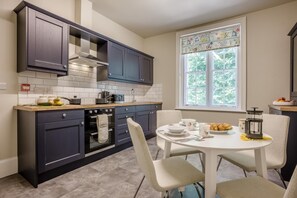 A modern kitchen with dark cabinets, a white countertop, and a dining area with a round table and chairs. - 3 Bed in Poole (oc-v45688) (Sandbanks)