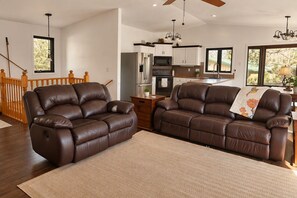 A living room with two brown leather recliners, a herringbone-patterned rug, and a view of the kitchen and dining area through an open doorway. - Waterfront Cabin - Private Dock, Kayaks, ATV & Snowmobile Trails (Bigfork)