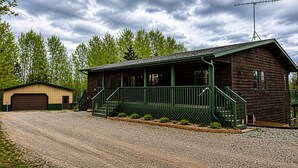 A wooden cabin with a porch, a garage, and a gravel driveway.