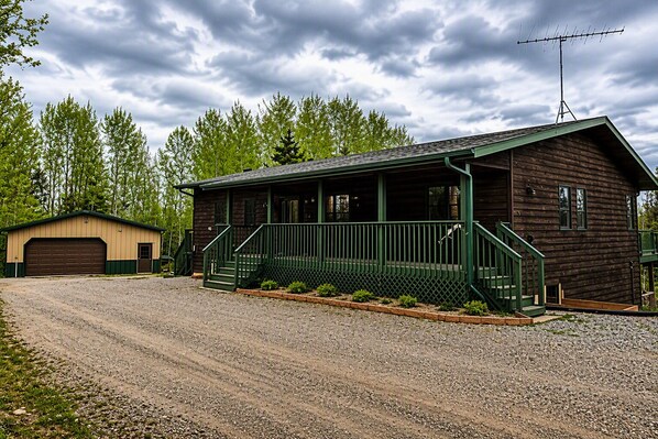 A wooden cabin with a porch, a garage, and a gravel driveway. - Waterfront Cabin - Private Dock, Kayaks, ATV & Snowmobile Trails (Bigfork)