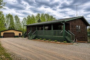 A wooden cabin with a porch, a garage, and a gravel driveway.