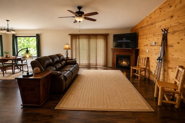 A cozy living room with a leather sofa, a fireplace, a television, and wooden walls.