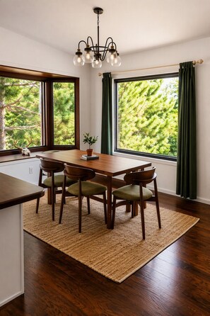 Un comedor con una mesa de madera, cuatro sillas, un tapete tejido y una araña.
