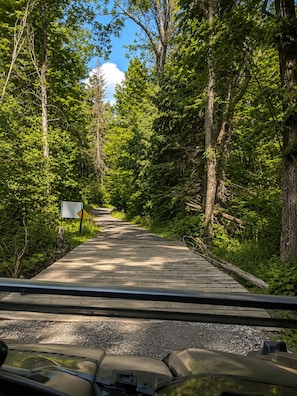 A wooden bridge in a forested area with a sign on the left.
