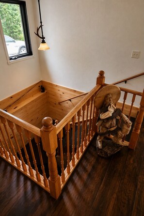 A wooden staircase with a railing, a small window with a view of greenery, and a hanging light fixture.