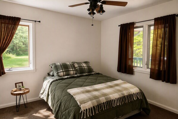 A bedroom with a bed, a ceiling fan, and windows with curtains.