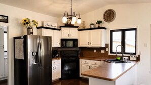 A modern kitchen with a stainless steel refrigerator, black stove, white cabinets, a wooden island with stools, and a window with a view.