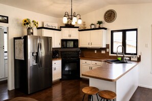 A modern kitchen with a stainless steel refrigerator, black stove, white cabinets, a wooden island with stools, and a window with a view.