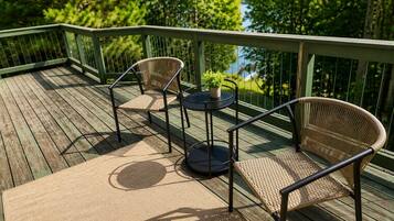 Une terrasse en bois avec deux fauteuils en osier et une petite table ronde, le tout entouré d’une rambarde en métal.