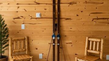 Un mur en bois, avec deux chaises en bois appuyées contre, et une paire de skis adossés au mur.