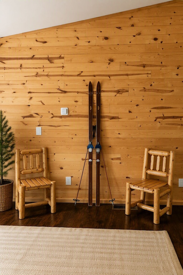 Una pared de madera con dos sillas de madera y un par de esquíes apoyados.