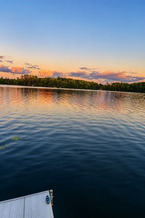 A calm lake with a dock extending into the water, surrounded by a forested shoreline.