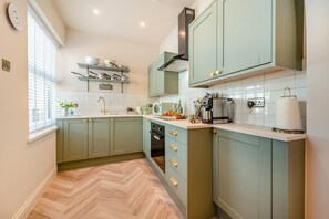 A kitchen with light green cabinets, a herringbone floor, a built-in oven, and a window with blinds. - 2 Bed in Saundersfoot (oc-s45875) (Saundersfoot)