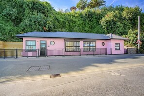 A pink building with a flat roof, a gated entrance, and a paved road in front. - 2 Bed in Saundersfoot (oc-s45875) (Saundersfoot)