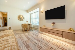 A modern bedroom with a large bed, a TV mounted on the wall, and a dining area with a table and chairs. - 2 Bed in Saundersfoot (oc-s45875) (Saundersfoot)