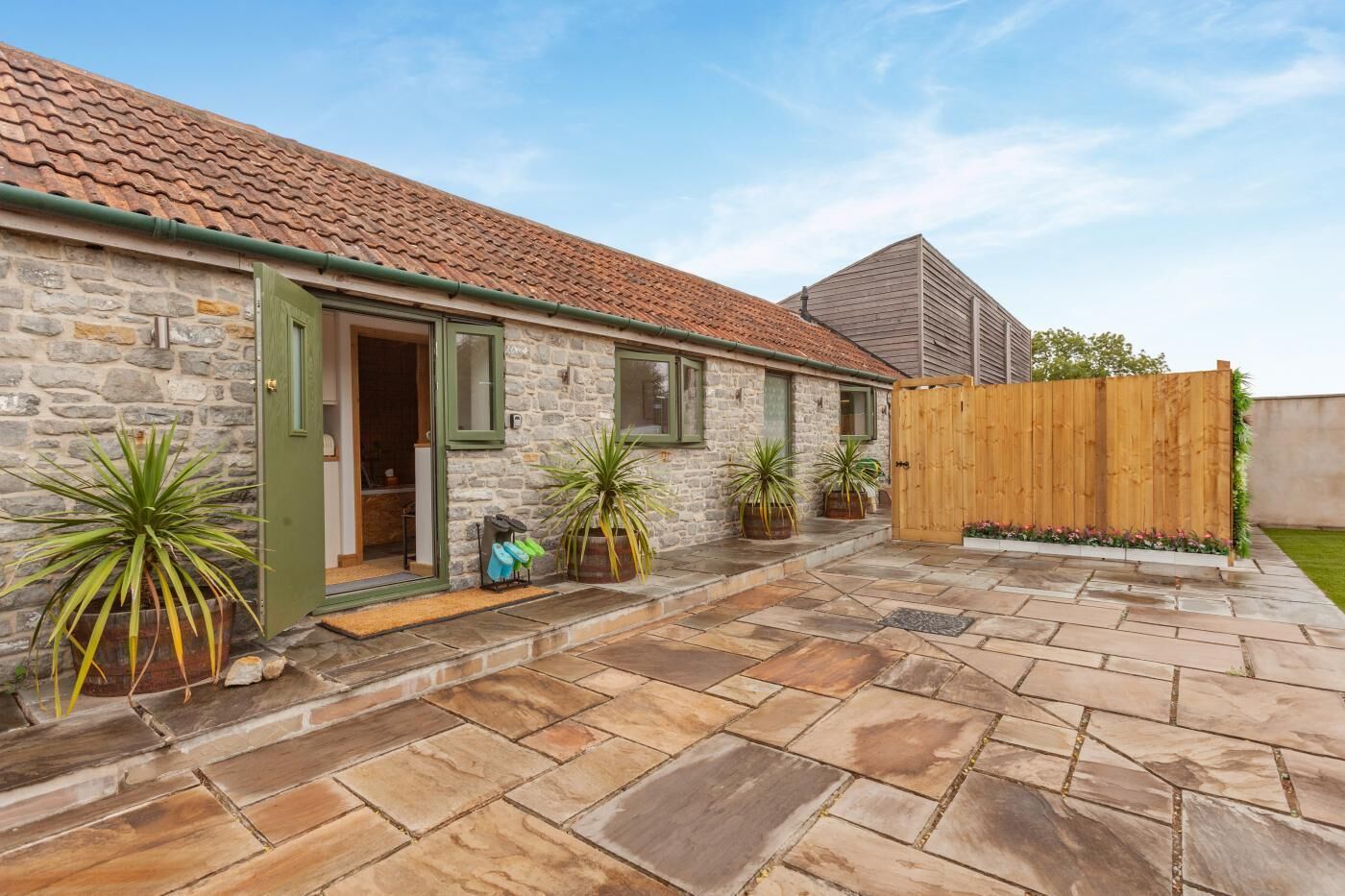A stone building with a tiled roof, a wooden fence, and potted plants.
