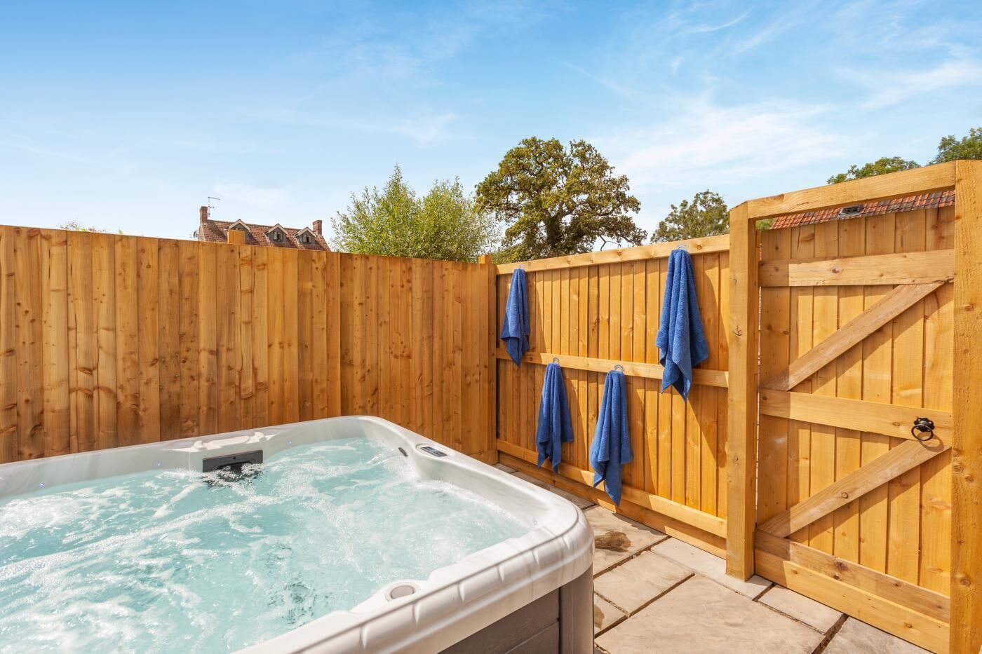 A hot tub in a wooden deck area with a wooden gate and towels hanging on the gate.